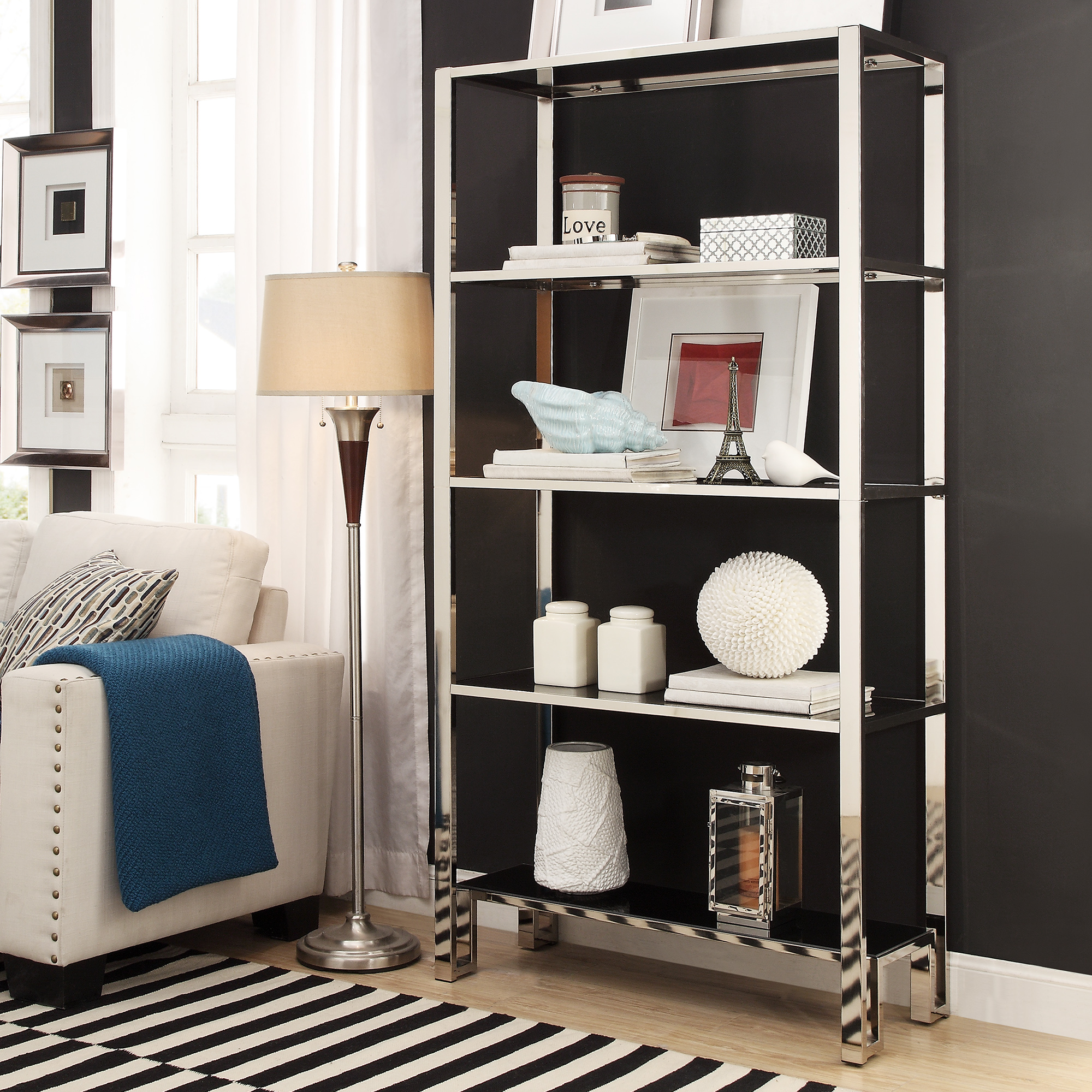 This chrome-finished bookcase is decorate with white and grey pieces of décor. These pieces are complemented by the chrome finish and a nearby white accent chair.