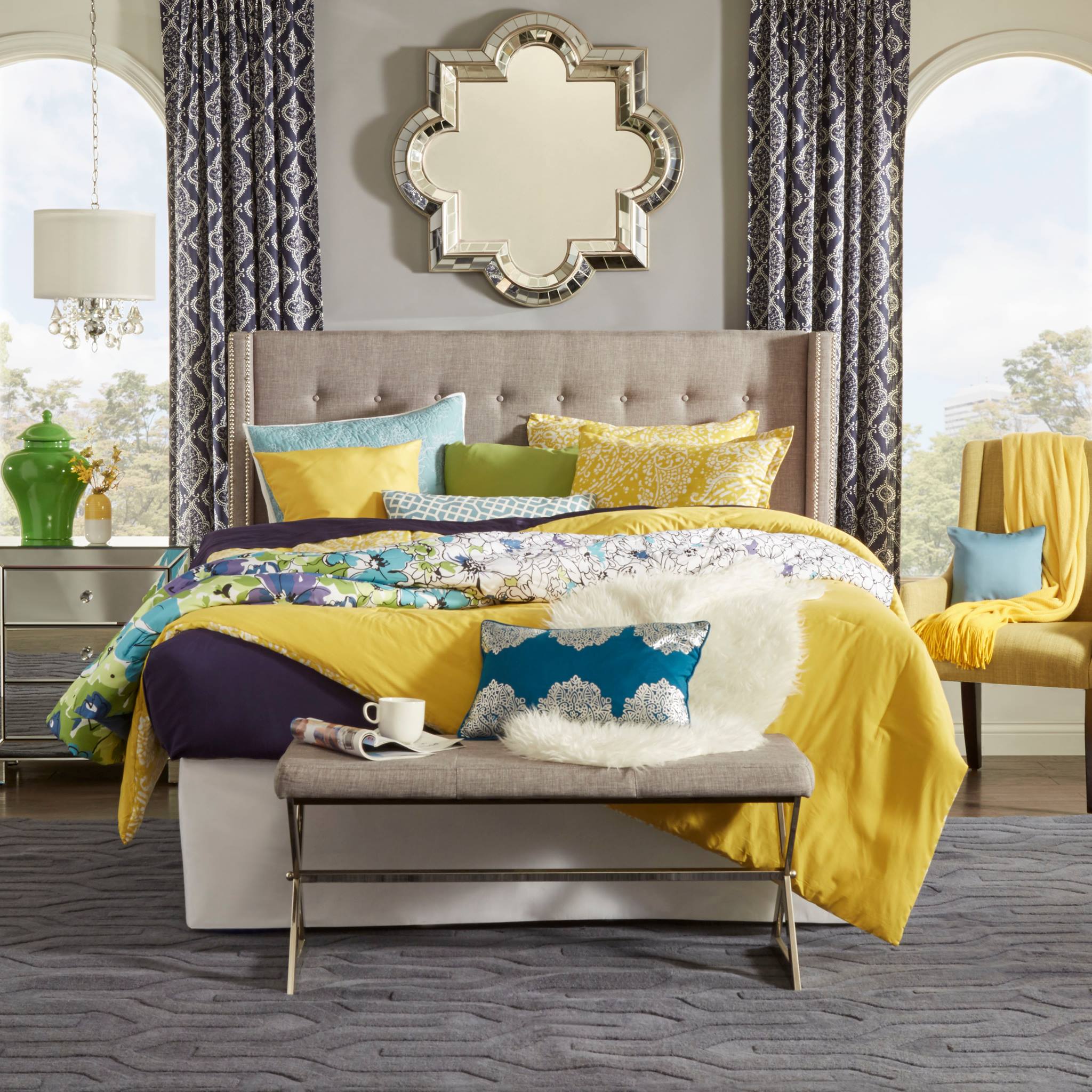 Pictured here is a bedroom with a feminine aesthetic full of a variety of colors. The beige linen upholstered button tufted wingback bed is dressed with sheets, blankets, and pillows in yellow, green, blue, and purple colors. There is a beige linen upholstered bench at the foot of the bed, which also has a pillow and blanket on.