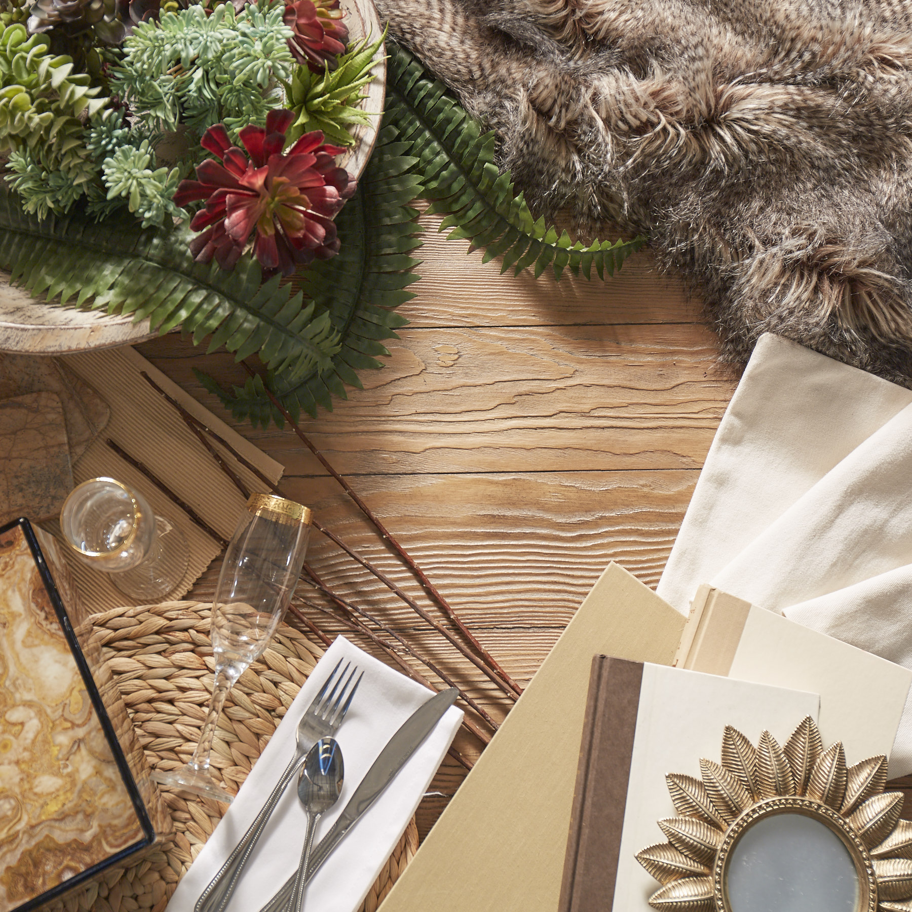 This image sets the mood for a modern and rustic space. It shows a top-down view of a wooden table, which is decorated with a variety of elements including paper, faux greenery, faux fur,  and some fabric.