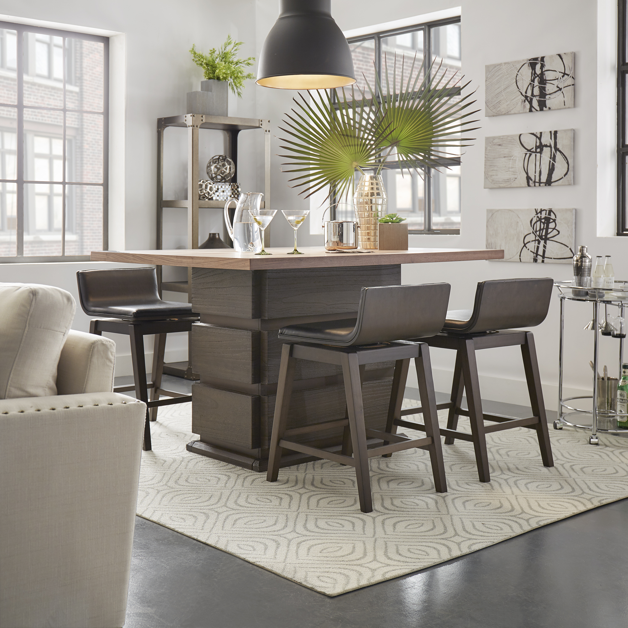 This one of our 10 inspiring dining combinations features a modern dining set. The dining table has a rectangular, dark brown pedestal base and a lighter brown wood table top. The four stools around the dining table have low backs and come in a dark brown finish that match the pedestal base. The table is decorated with gold and clear glassware.