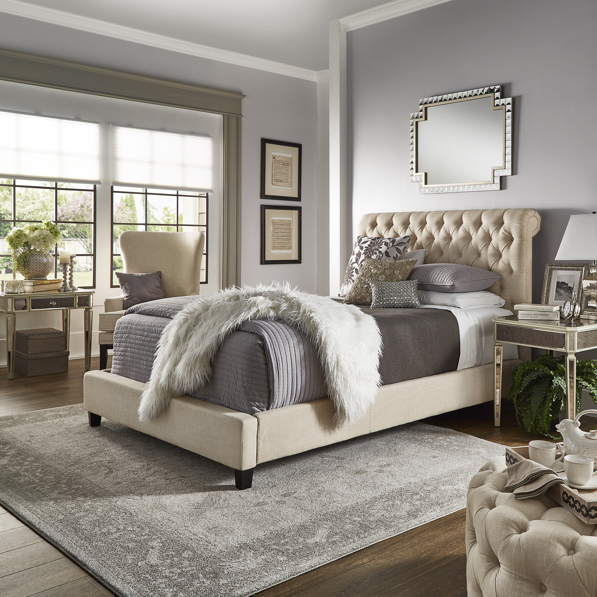 This last image features a chesterfield-inspired bed. There is button tufted beige linen upholstery and a rolled top headboard. The bed is elegantly dressed with grey and white bedding.