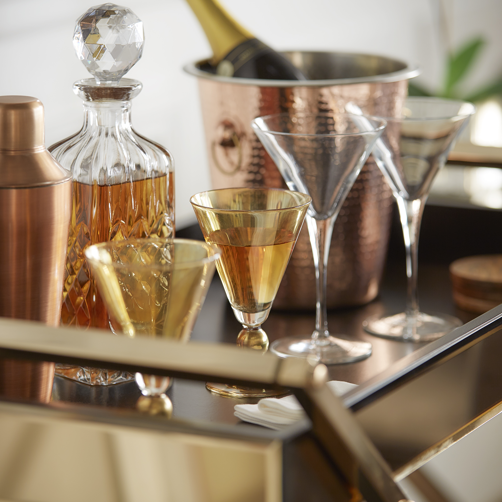 Another closeup view of another bar cart. This bar cart has a shiny champagne gold finish and has the top shelf decorated with gold, orange, and copper barware.