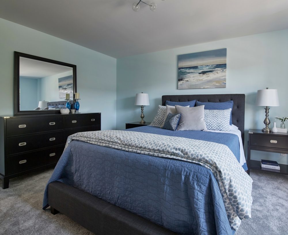 In the final bedroom in the house, there is a dark grey linen upholstered bed. The two nightstands featured a black finish and matched the black dresser and mirror.