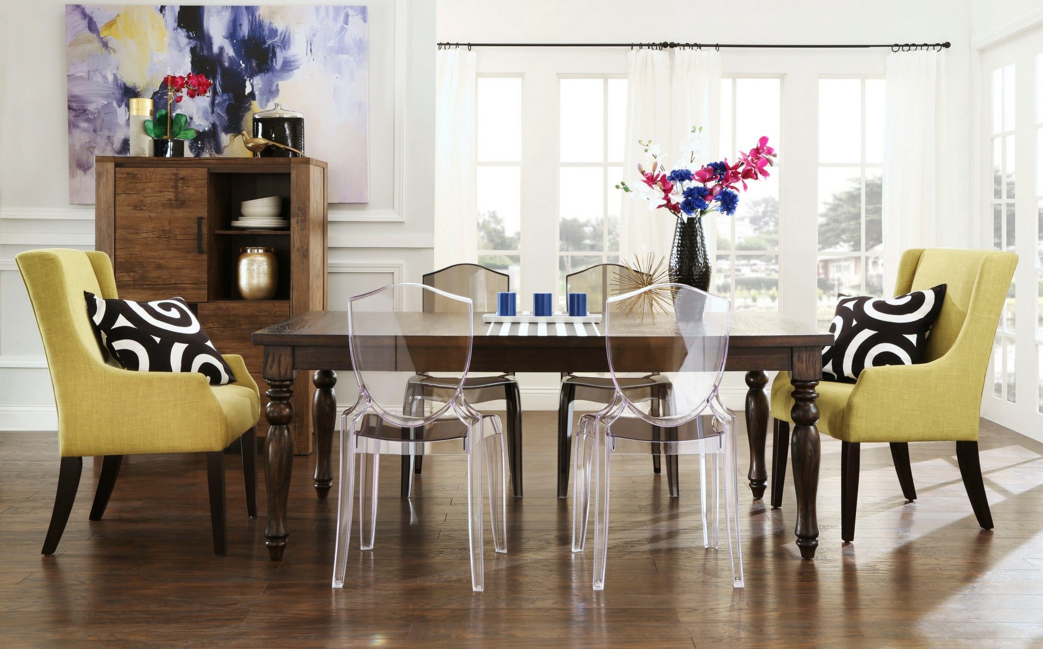 This eclectic mix features a traditional wood dark brown rectangular dining table. There are four clear acrylic dining chairs and two light green hostess chairs, one on each end of the table. Black and white accessories decorate the dining set.