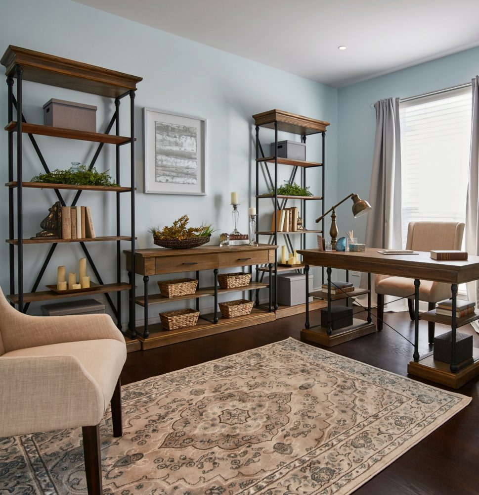 The home office in this house has rich, dark brown floors with light blue walls. The bookcases, console table, and desk all match and feature black metal frames and light brown wood surfaces.