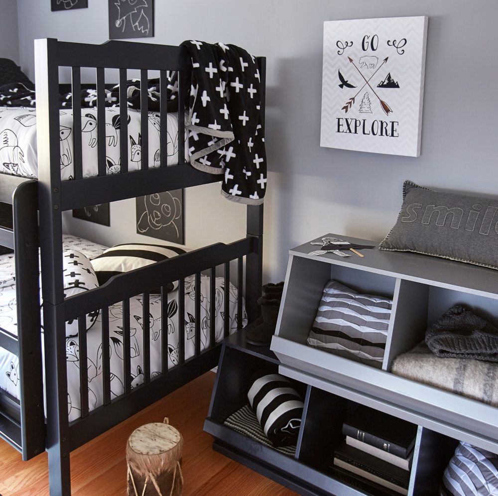 On the other side of the bedroom, we have a black finished bunk beds and some stackable modular storage bins. The beds are dressed with fox-printed sheets and black and white pillows and blankets. The storage bins are black and grey, and filled with spare blankets, pillows, and books.