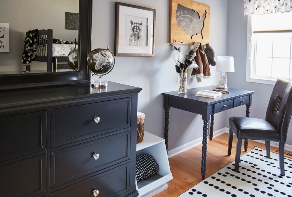 A wider view of one side of the kids bedroom. It includes the black desk, faux leather parsons chair, and white modular stackable storage bin. However, the image also shows a black finished dresser and mirror. 