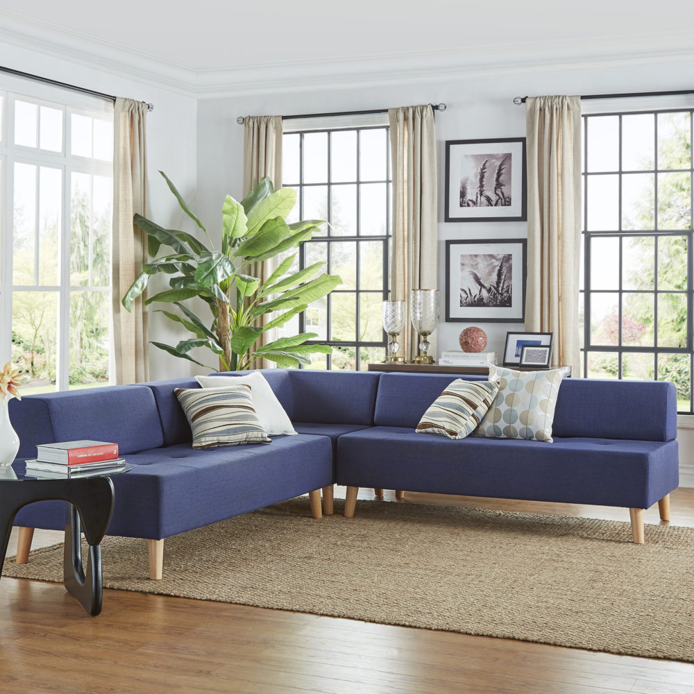 Pictured is a living room with a twilight blue linen upholstered armless sectional sofa in the center. The sofa is minimally decorated with four accent pillows, each featuring a blue and brown print.