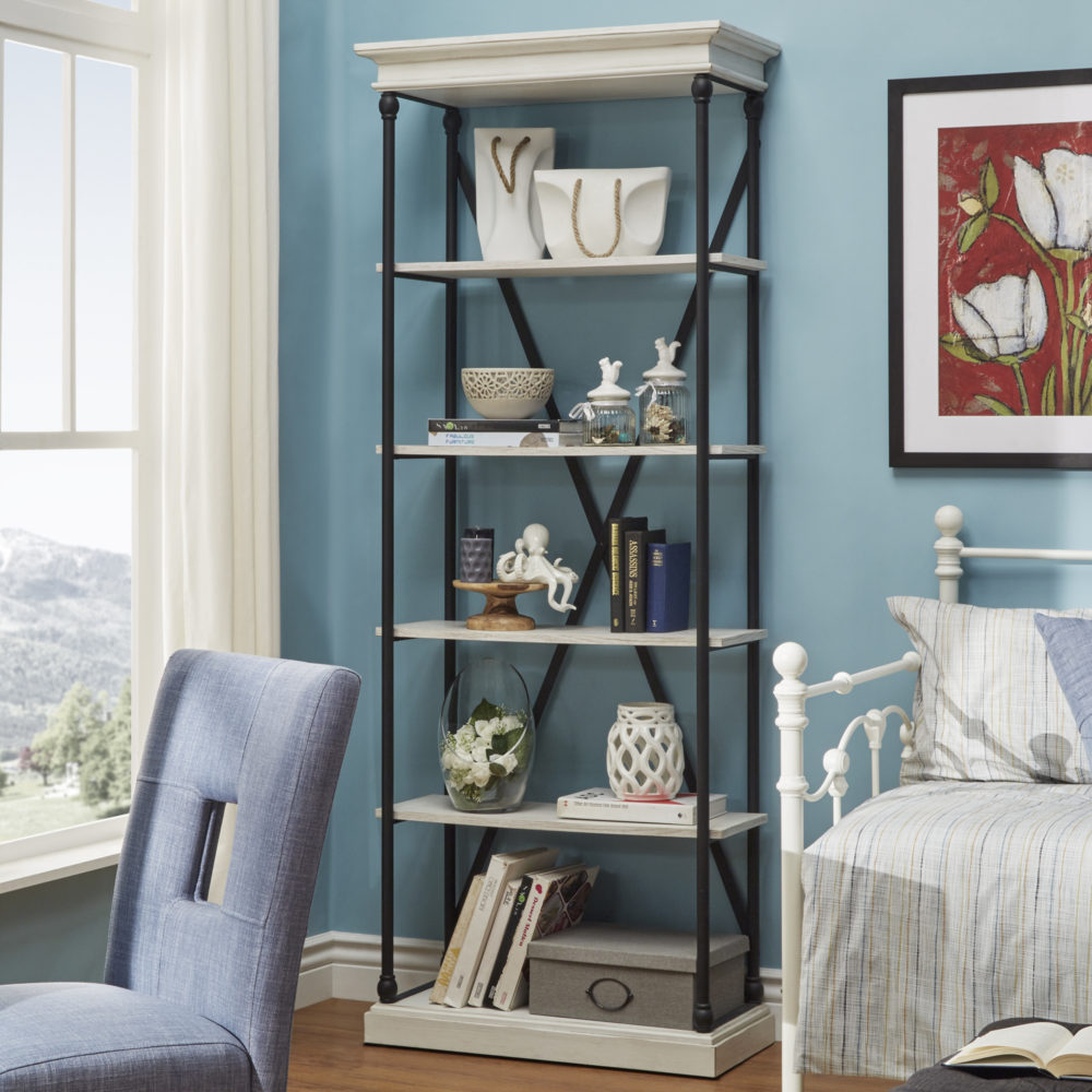 This is the iNSPIRE Q Cornice Etagere Bookcase in an ivory white finish. This bookshelf is decorated with various pieces of décor and books in different shades of white, grey, black, and blue. The colors really stand out against the light blue walls, ivory white finish of the shelves, and the white metal daybed off to the side. 