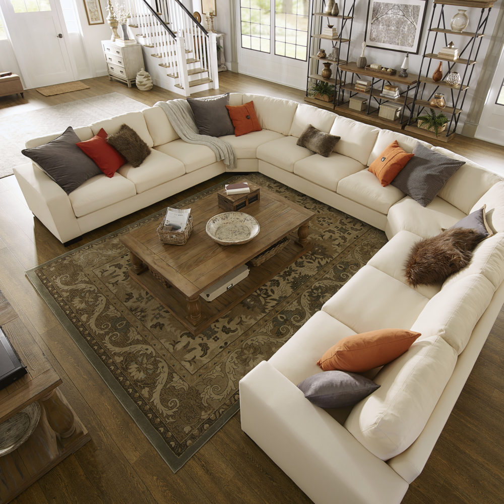 This last view of our classic-styled space has a different sofa. In the heart of the room is a U-shaped sectional sofa upholstered in white fabric. With a bigger, plusher sofa, there is more room for more throw pillows, so there are plenty of brown and orange pillows to go around. In the center of the U-shape is the rectangular wood coffee table. 