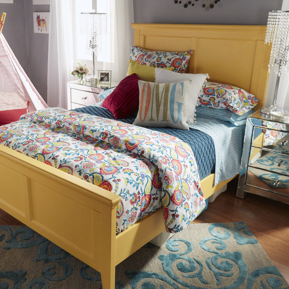 Another one of our kids and teen bedroom ideas features this wood panel bed that comes in a sunny yellow finish. The bedding is primarily blue, with white, grey, red, and green accents. The look is lively and playful. The two nightstands are mirrored and have 3 drawers to enhance the bright colors of the bed.