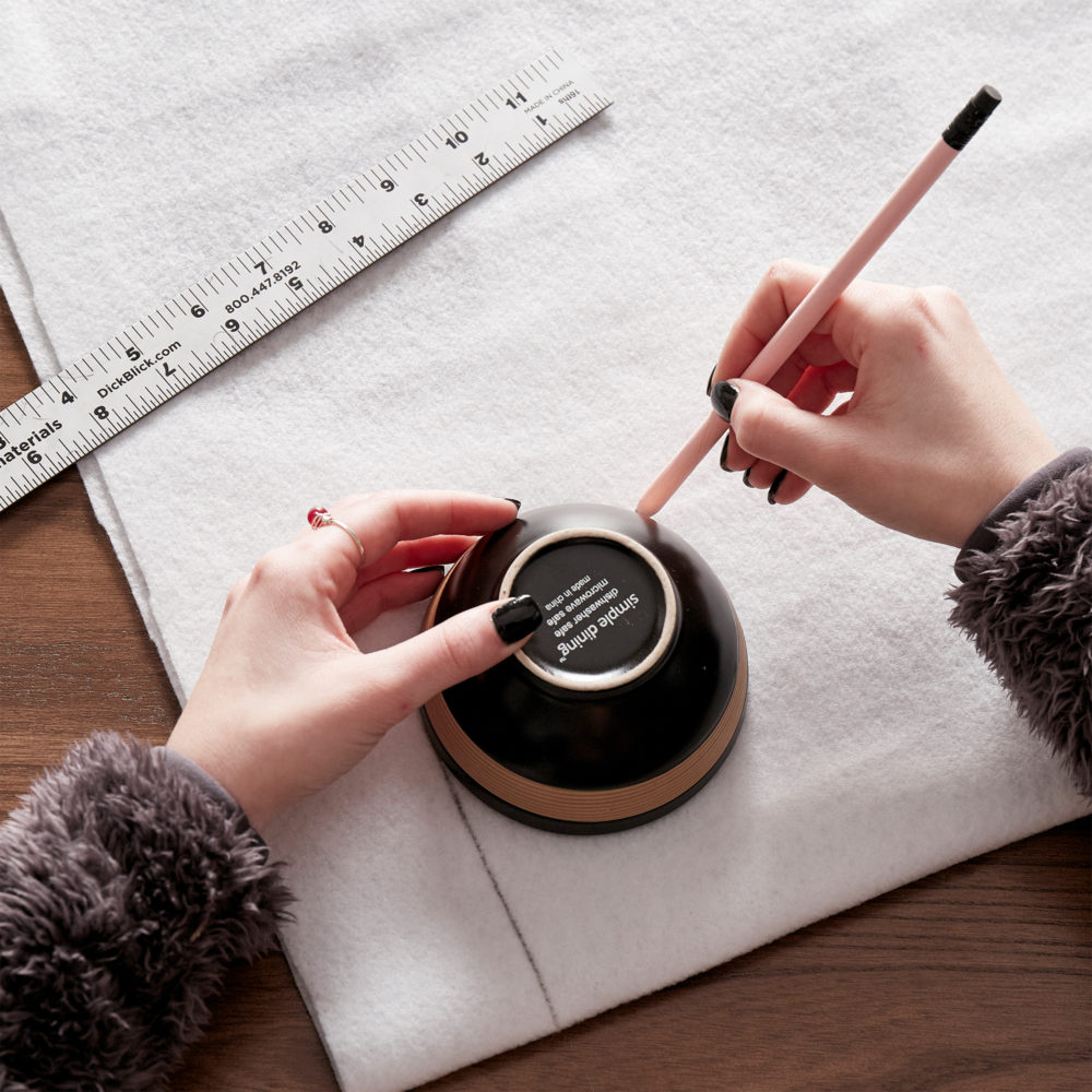 In this image, our designer uses a small bowl to draw a perfect half circle on the white fabric to begin making the DIY Valentine's Day table.