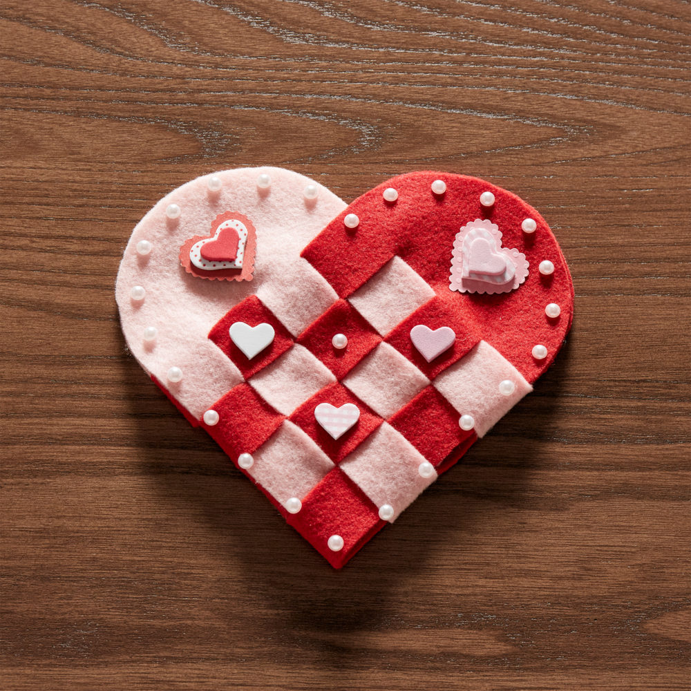 This image shows the complete DIY Valentine's Day table décor. The woven fabric heart has two tones to it, pink and red, with smaller hearts and white pearls decorating it.