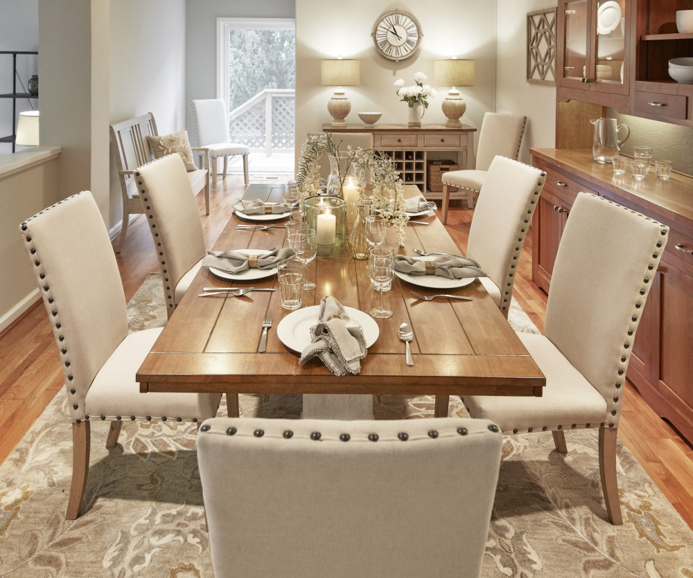 This is another view of our formal dining room from the head of the table. We see the six table settings on the oak finished table top. There are six beige linen upholstered dining chairs, all with bronze nailhead trims.