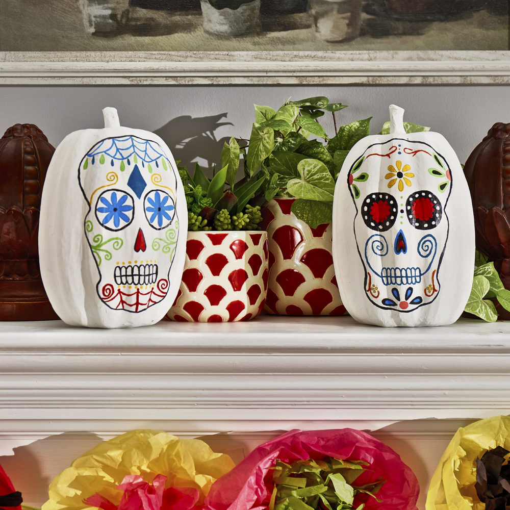 This is one of our Day of the Dead décor ideas. This image shows two white pumpkins painted like calaveras de azucar sitting atop a fireplace mantle.