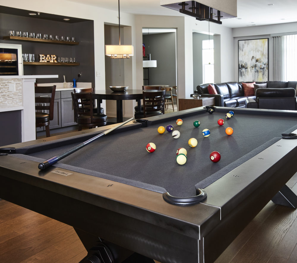 A pool table is prominently displayed with a home bar and leather sofa is featured in the background.