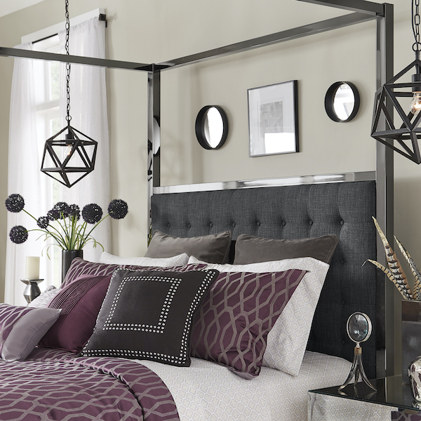 Last, but not least, this modern canopy bed is quite similar to the bed with the bonded leather upholstery. Instead, this bed has dark grey linen upholstery for the headboard, complete with button tufting. The metal frame has a black nickel finish, while the bedding is full of rich hues of purple, grey, and black. The white sheets offset the dark colors beautifully.