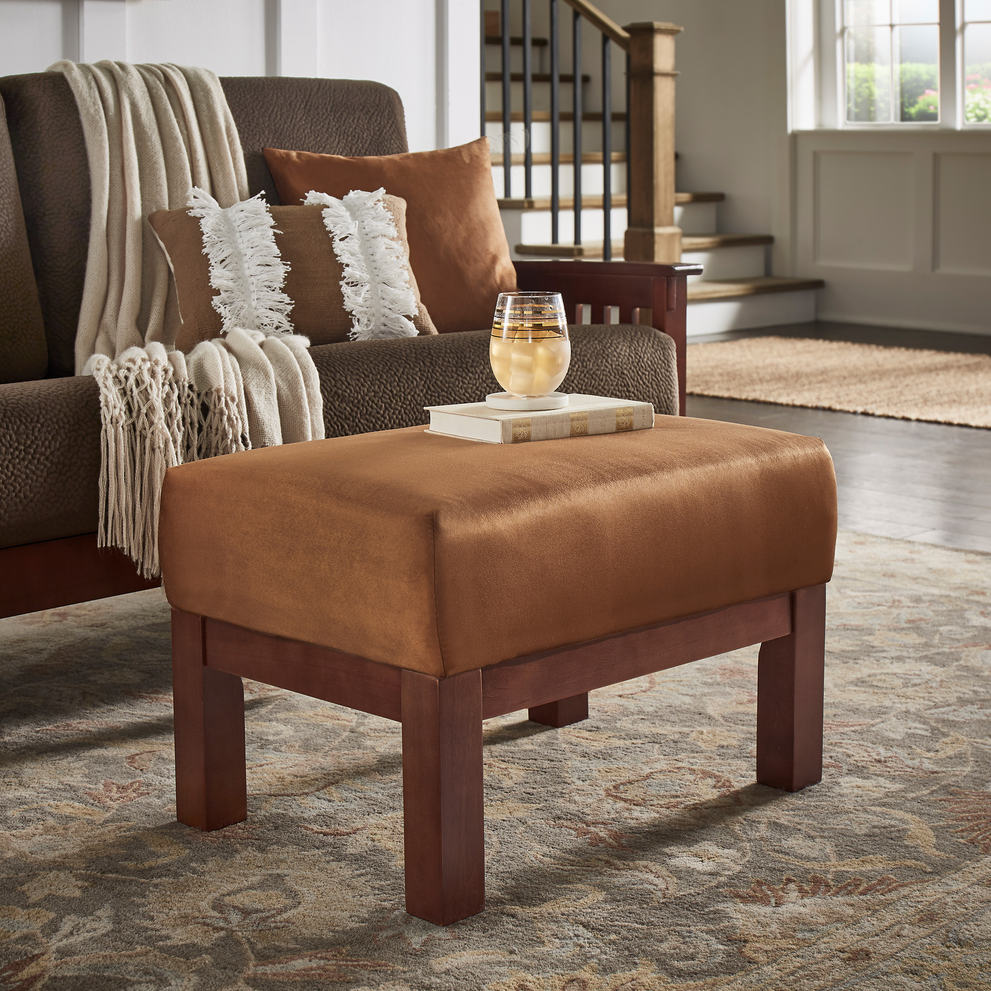The final fabric we discuss is microfiber. Pictured here is the Mission-Style Oak Finish Wood Ottoman in Rust Microfiber Upholstery by iNSPIRE Q Classic. Perched atop the ottoman is a single book and a glass of iced tea.