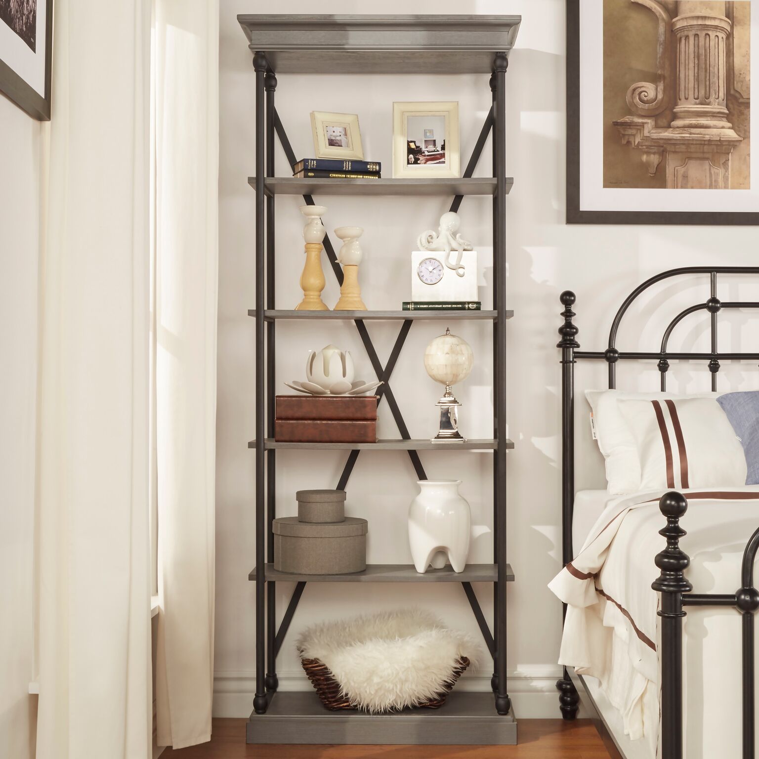 To illustrate etagere design, this image shows the Cornice Etagere Bookcase by iNSPIRE Q Artisan in a grey finish. The bookcase is placed next to a bed and is decorated with home accessories. With the etagere design, all eyes go to the décor displayed.