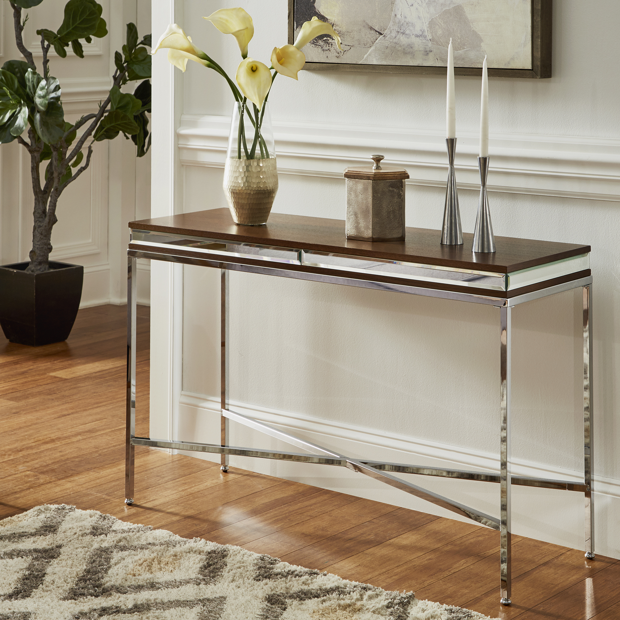 This is the Mirror Trim Sofa Table in Chrome Finish by iNSPIRE Q Bold. It is placed in a hallway with a few pieces of décor on display.